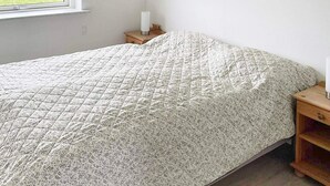 Un dormitorio con una cama, una mesita de noche, un ventanal y dos obras de arte colgadas en la pared.