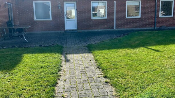 Un edificio de ladrillo con techo de tejas, entrada pavimentada y césped.