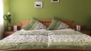A bedroom with a green wall, two framed pictures, a wooden headboard, a bed with patterned bedding, a bedside table with a lamp, and a clock displaying 15:38. - Philipps Holiday Apartment (Graach)