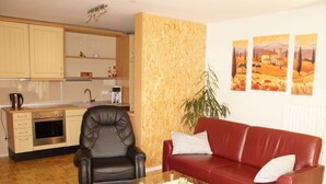 A compact living space with a kitchenette, a leather armchair, a red sofa, and a glass coffee table. - Philipps Holiday Apartment (Graach)