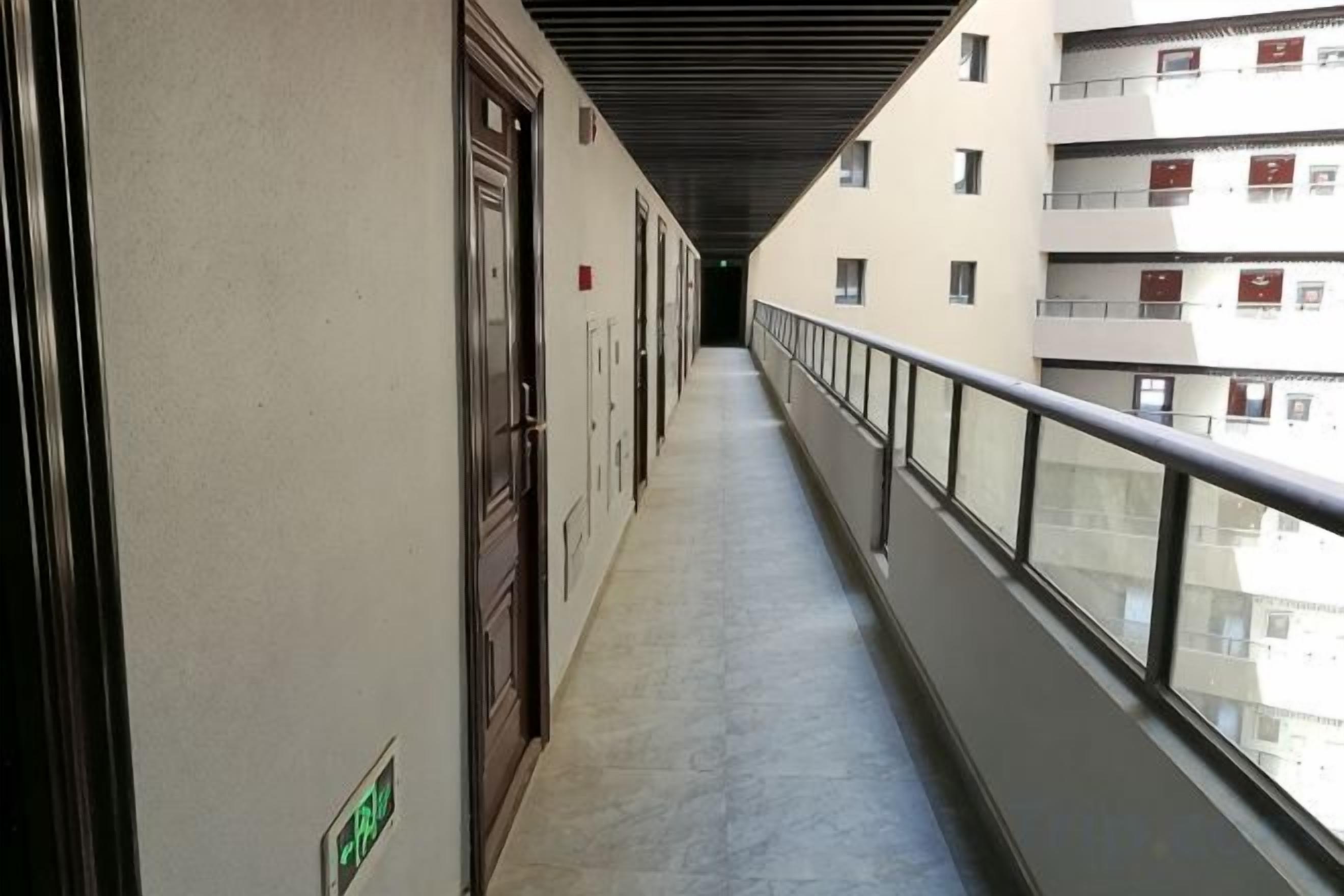 A corridor with doors, a railing, and a view of a building with multiple floors.