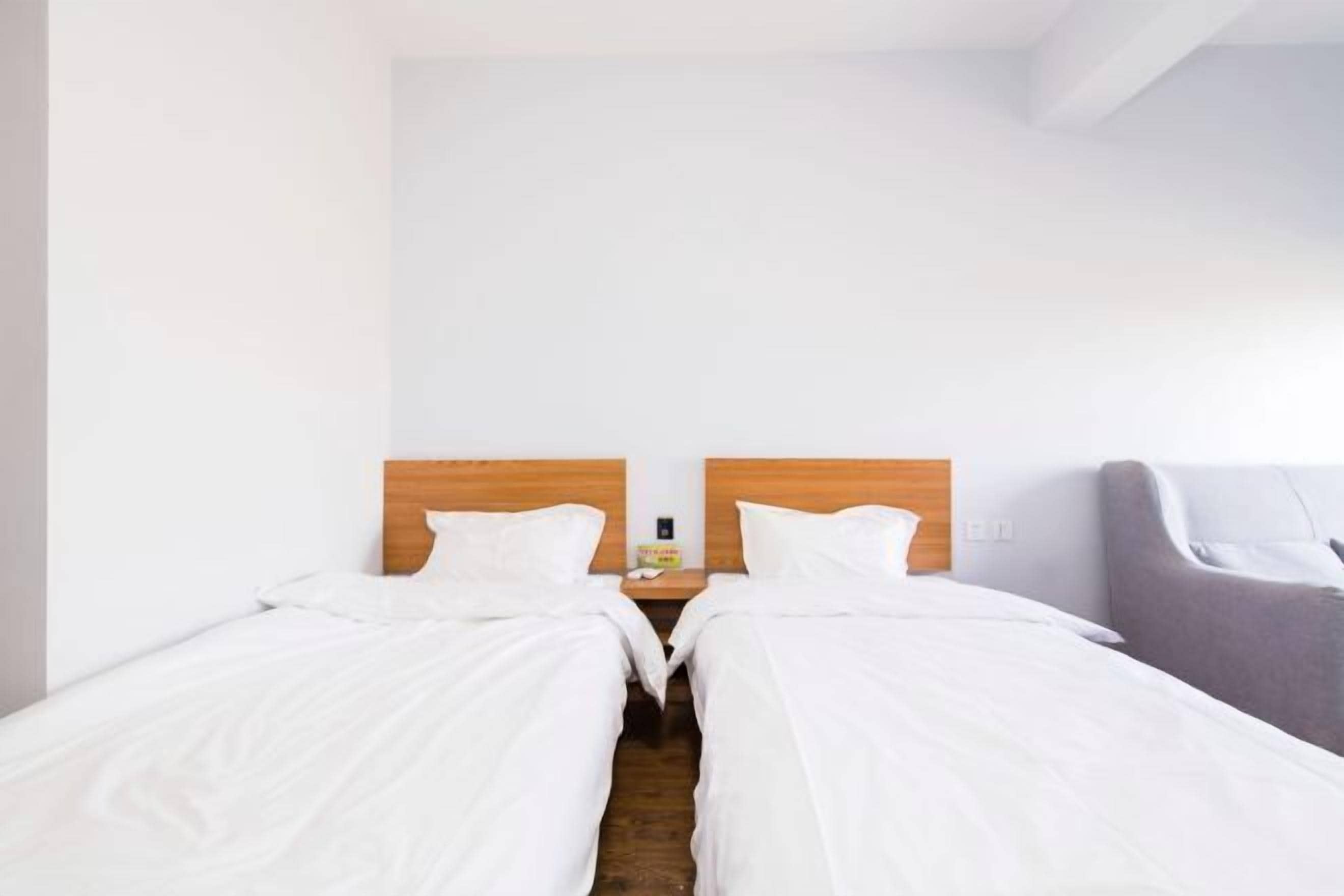 Habitación doble con dos camas, cabeceros de madera, una mesita de noche y un sillón gris.