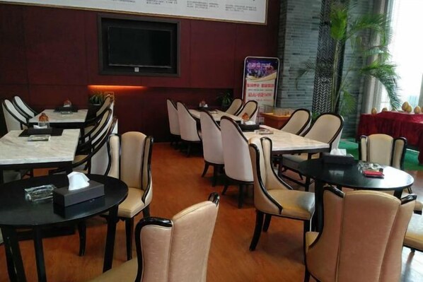 A restaurant with multiple tables and chairs, a television mounted on the wall, and a menu stand.