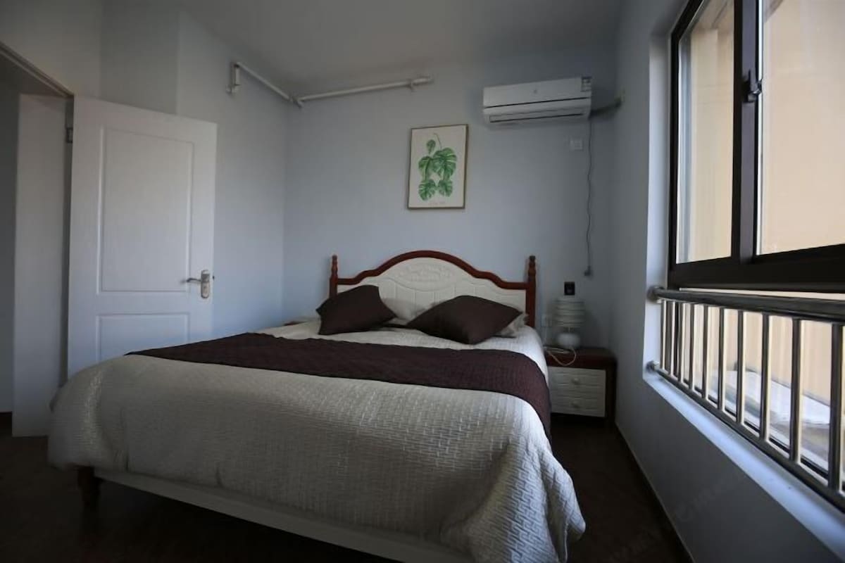 Een slaapkamer met een bed, nachtkastje, een wandairconditioner, een raam met uitzicht en een deur.