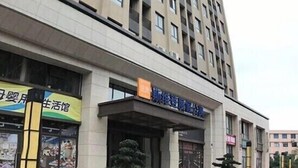 A tall, modern building with a curved facade, featuring a ground-level entrance with signage. - Hangzhou Tonglu Shengtuo Serviced Apartment (Tonglu East Station Jiangnan Town) (Tonglu)