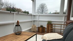 Ein gemütlicher Balkon mit Holztisch, gepolstertem Sofa und Topfpflanzen.