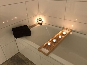 Ett badrum med ett badkar, ett träbricka med ljus och en svart handduk.