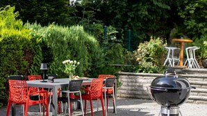 An outdoor patio with a table and chairs, a barbecue grill, and a fountain in the background. - Maria Luise Comfortable Holiday Residence (Bad Harzburg)