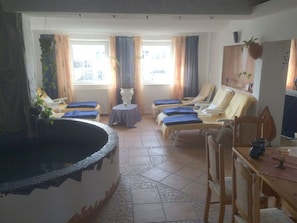 Un cuarto de spa con hidromasaje, sillones de masaje y una pequeña mesa con una planta.