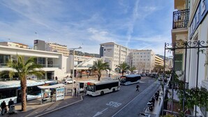 A street view with a bus stop, palm trees, and a building with balconies. - HOTEL DU NORD (Cannes)