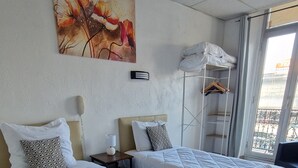 A hotel room with two beds, a painting on the wall, a window with a view, and a wooden floor. - HOTEL DU NORD (Cannes)