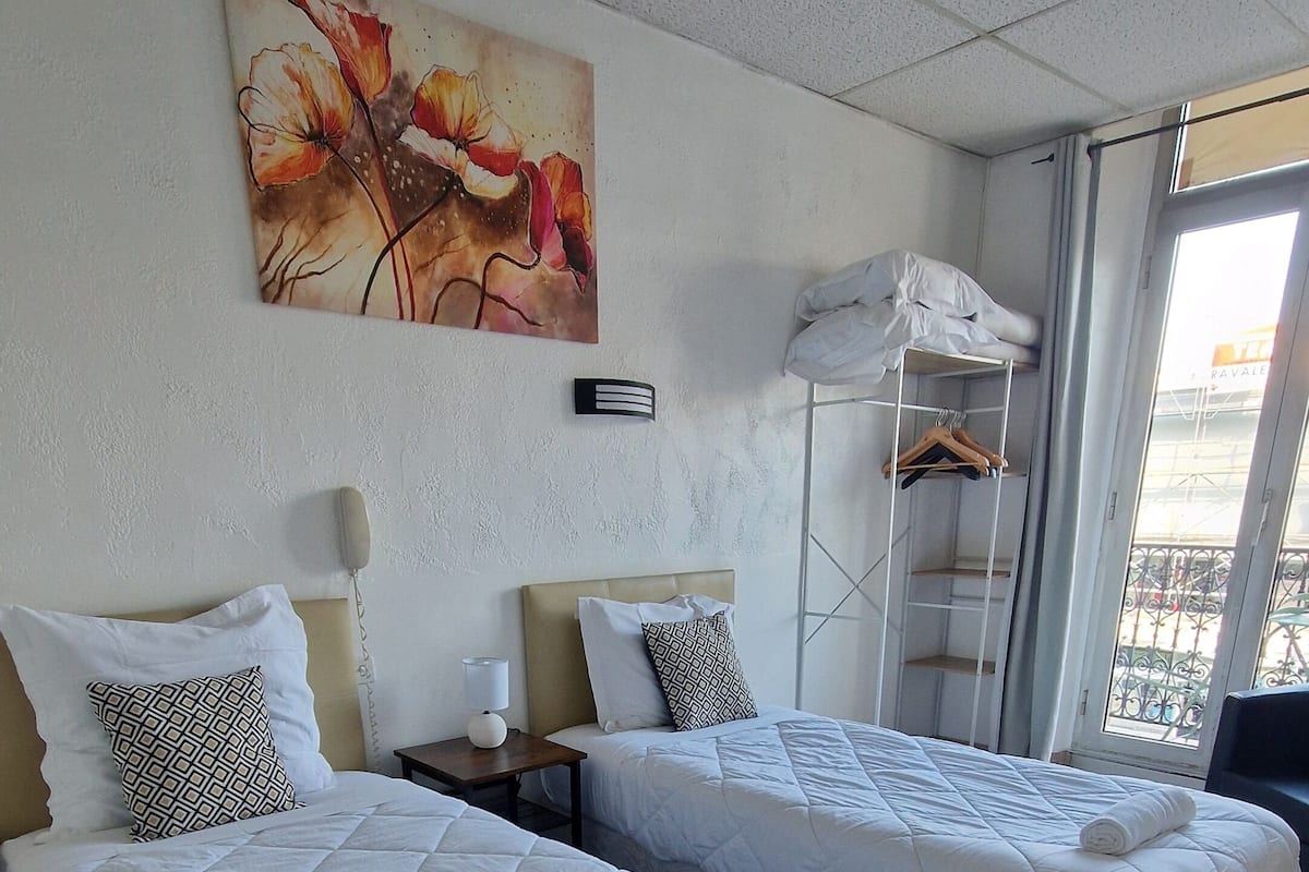 A hotel room with two beds, a painting on the wall, a window with a view, and a wooden floor.