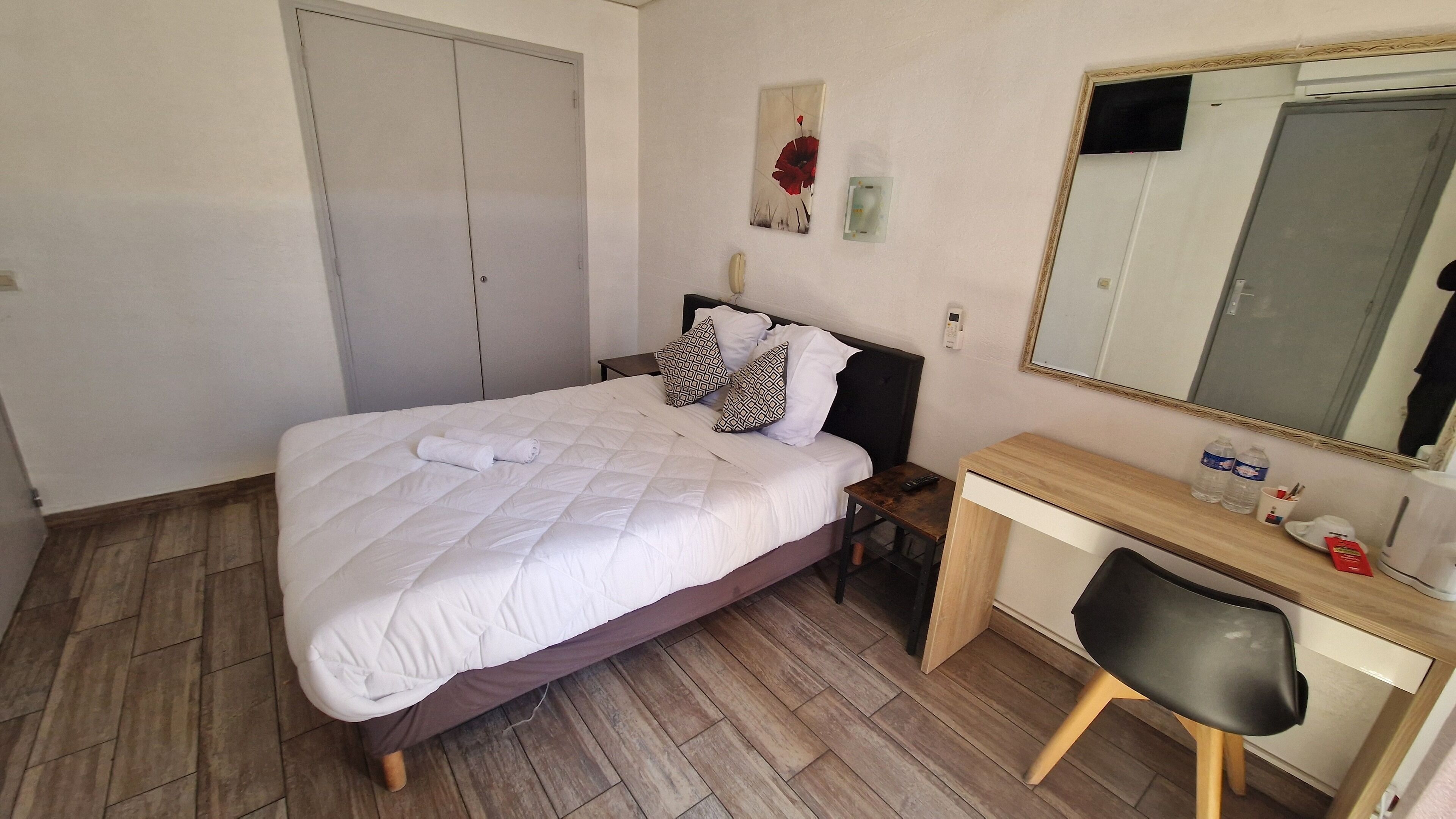 Een keurig opgemaakt slaapkamer met een bed, nachtkastje, stoel, bureau en spiegel.