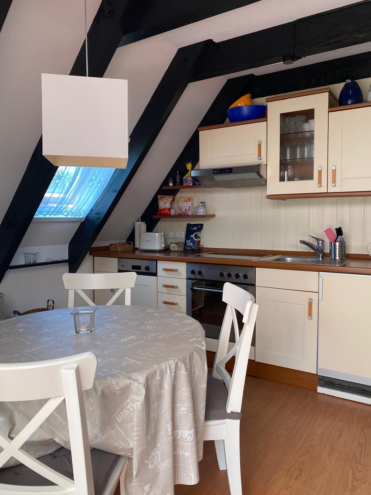 Une cuisine chaleureuse avec un coin repas, caractérisée par un plafond en pente, des poutres en bois et un puits de lumière.