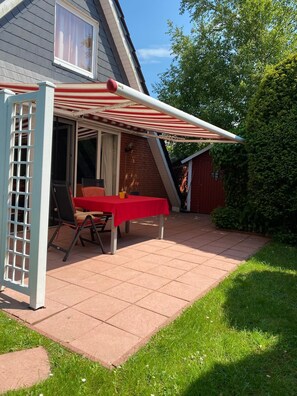 Eine Terrasse mit einem roten Tisch und Stühlen, einem weißen Sonnenschirm und einer Ziegelwand.