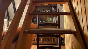 Una scala in legno con un lucernario in cima, che conduce a una stanza con una libreria e vista sul cielo.