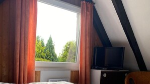 Una camera da letto con un letto grande, una finestra con tende, una televisione su un supporto e una sedia.