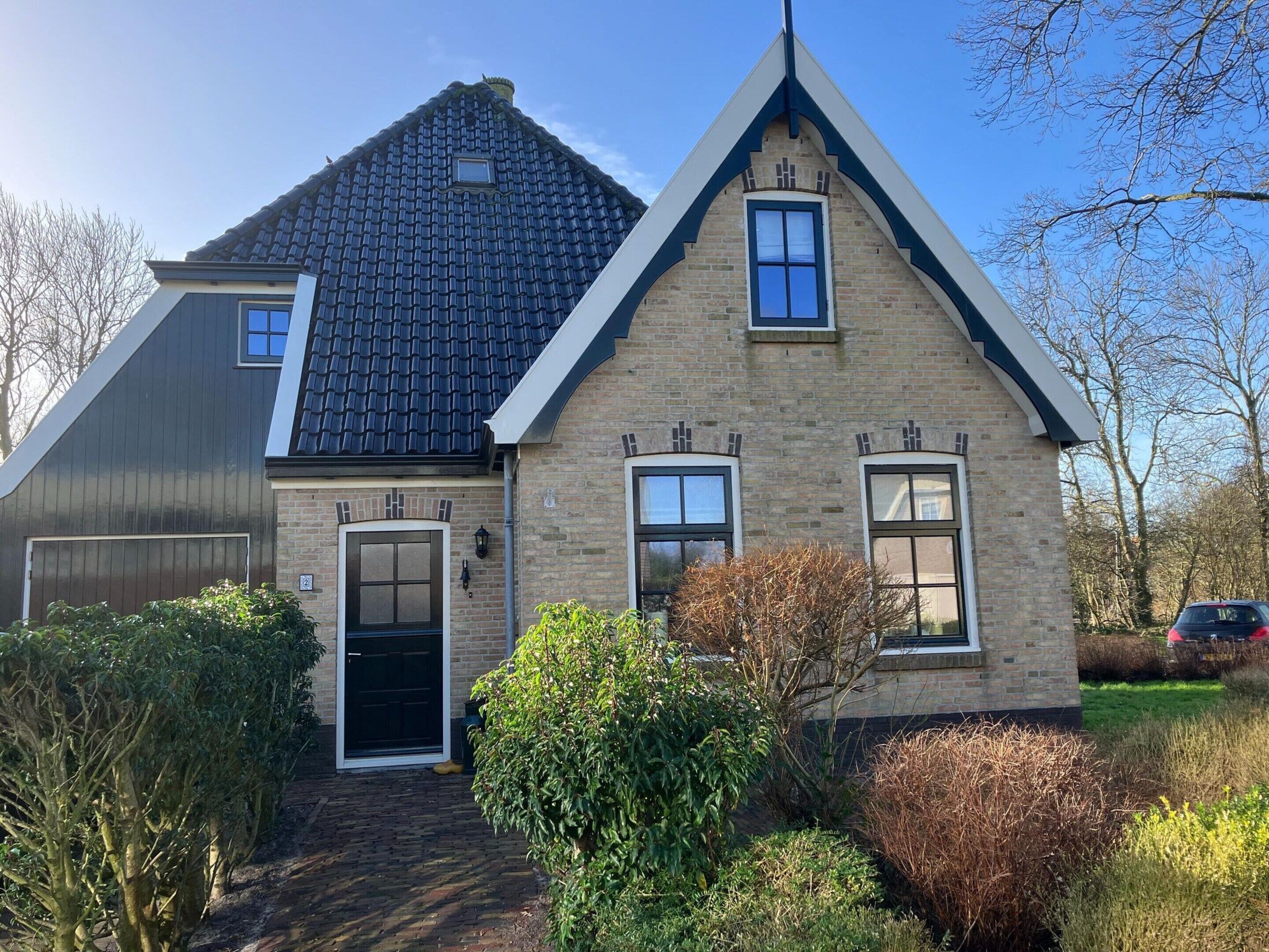 A two-story house with a dark tiled roof, a brick facade, and a front door.
