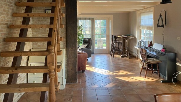 Ein geräumiger Raum mit einer Holztreppe, einem Klavier und einem Essbereich mit Stühlen und einem Tisch.