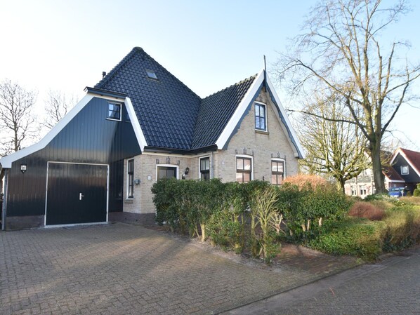 A two-story house with a steeply pitched roof, a garage, and a paved driveway. - Spacious Holiday Home Close to the sea (Burgerbrug)