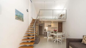 Eine moderne Wohnung mit einer Holztreppe, einem Essbereich mit Tisch und Stühlen, einem Sofa und einer Küche im Hintergrund.