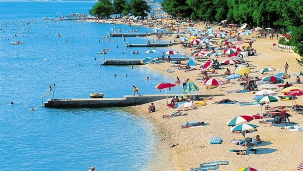 Ein voller Strand mit vielen Sonnenschirmen und Menschen, die im Wasser entspannen.