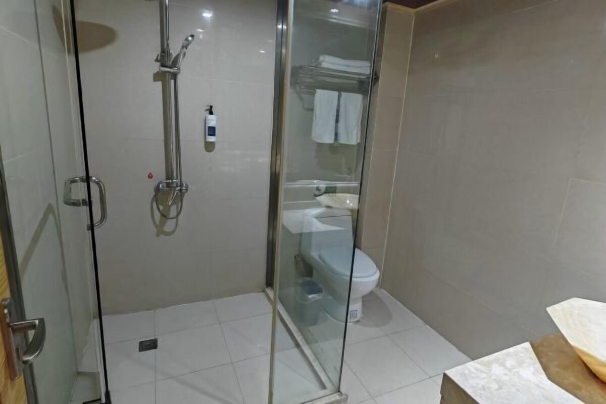 Área de chuveiro com box de vidro, chuveiro manual e torneira embutida na parede.