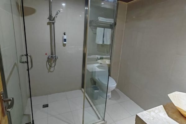Área de chuveiro com box de vidro, chuveiro manual e torneira embutida na parede.