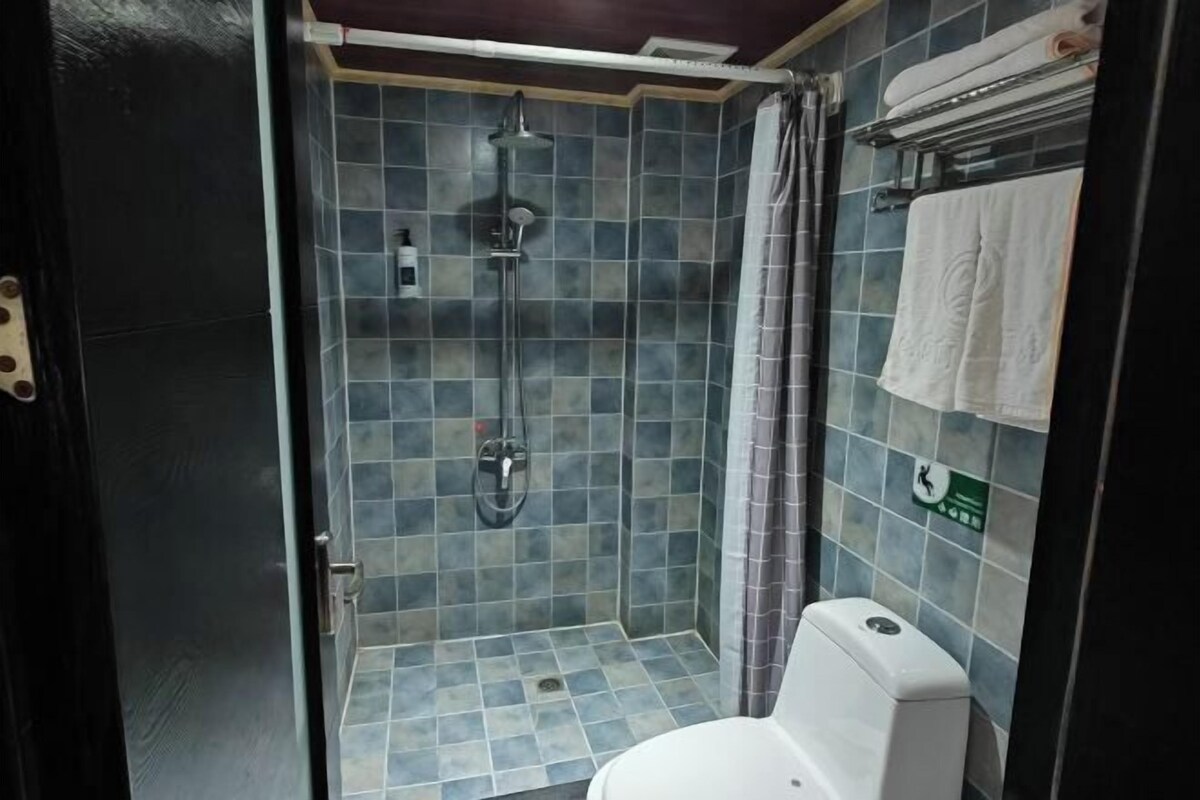 Casa de banho pequena, com azulejos, chuveiro, sanita e porta-toalhas.