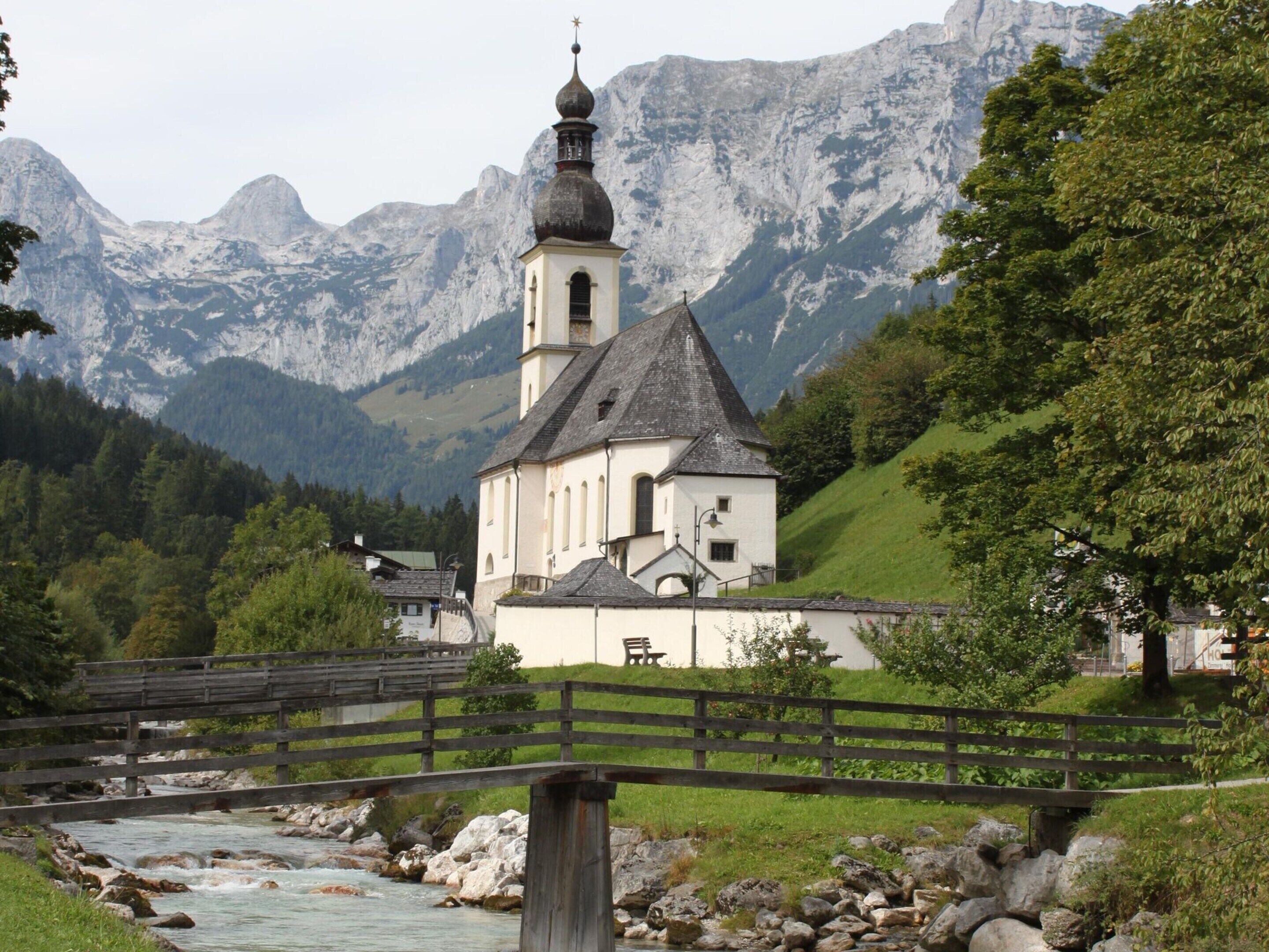 A church with a bell tower, surrounded by mountains and a river.