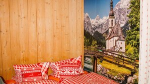 Ein Schlafzimmer mit einer Holzwand, einem Bett mit rot-weißer Karomattraze und einem Wandbild von einer Berglandschaft mit einer Kirche.