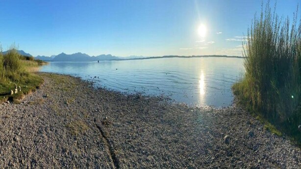 Ein ruhiger See mit blauem Himmel und Bergen in der Ferne.