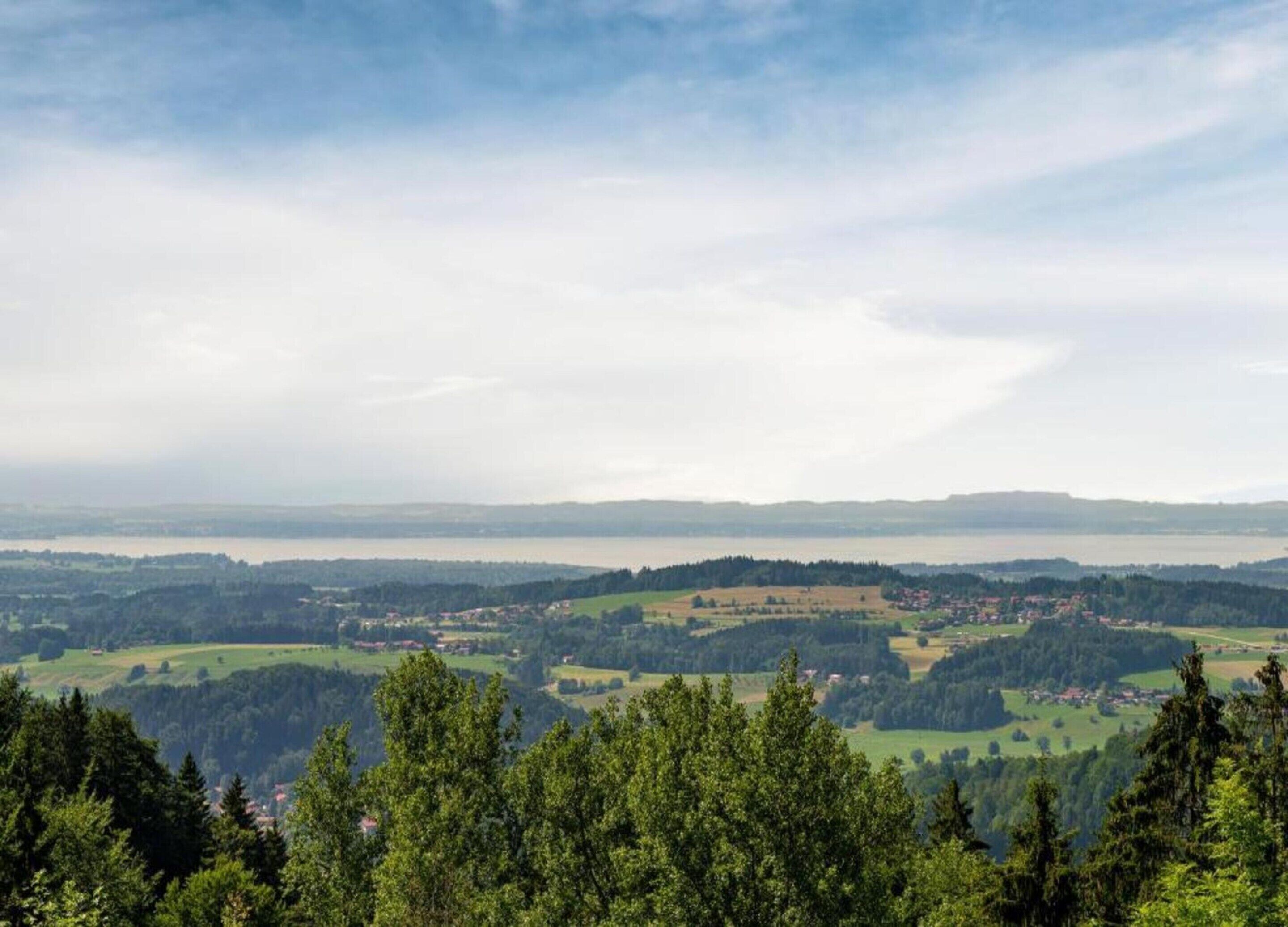 A panoramic view of a mountainous landscape with a lake in the distance, surrounded by forested areas and scattered settlements.