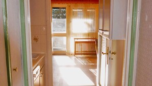 Ein schmaler Flur, der zu einem Raum mit einer hölzernen Bank und einem fenster mit Vorhängen führt.
