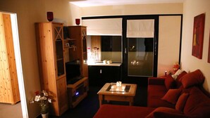 A cozy living room with a red sofa, wooden entertainment unit, and a dining table with candles. - Ostseeliebe Comfortable Holiday Residence (Schönberg)