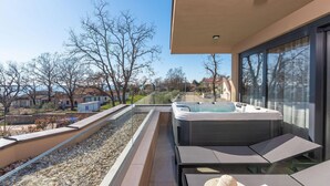 A balcony with a hot tub, seating area, and a view of the neighborhood.