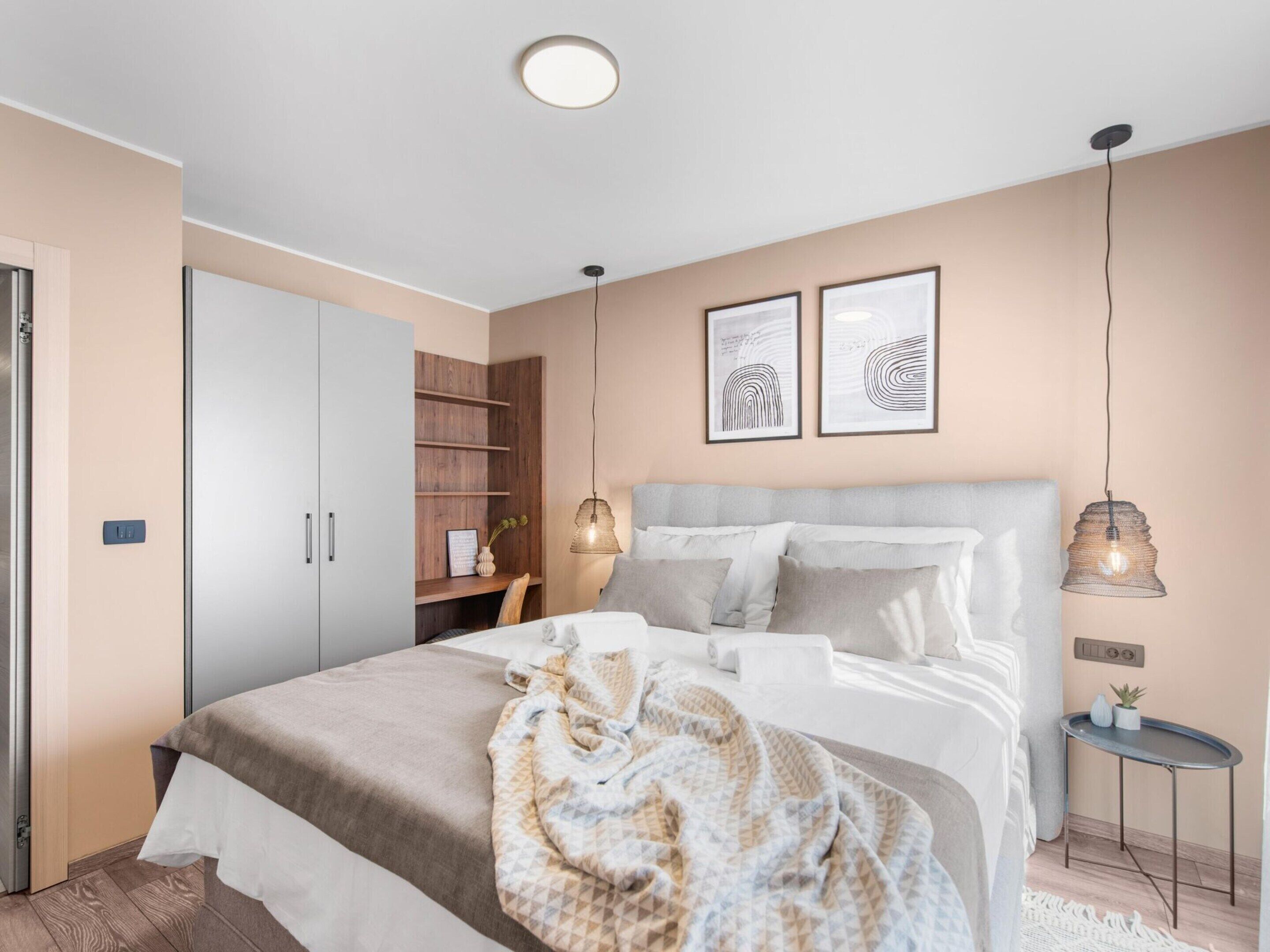 Un dormitorio moderno con cama, mesitas de noche, armario y cuadros en la pared.