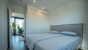 Quarto com uma cama grande, cabeceira cinza e vista para o exterior através de uma porta deslizante.