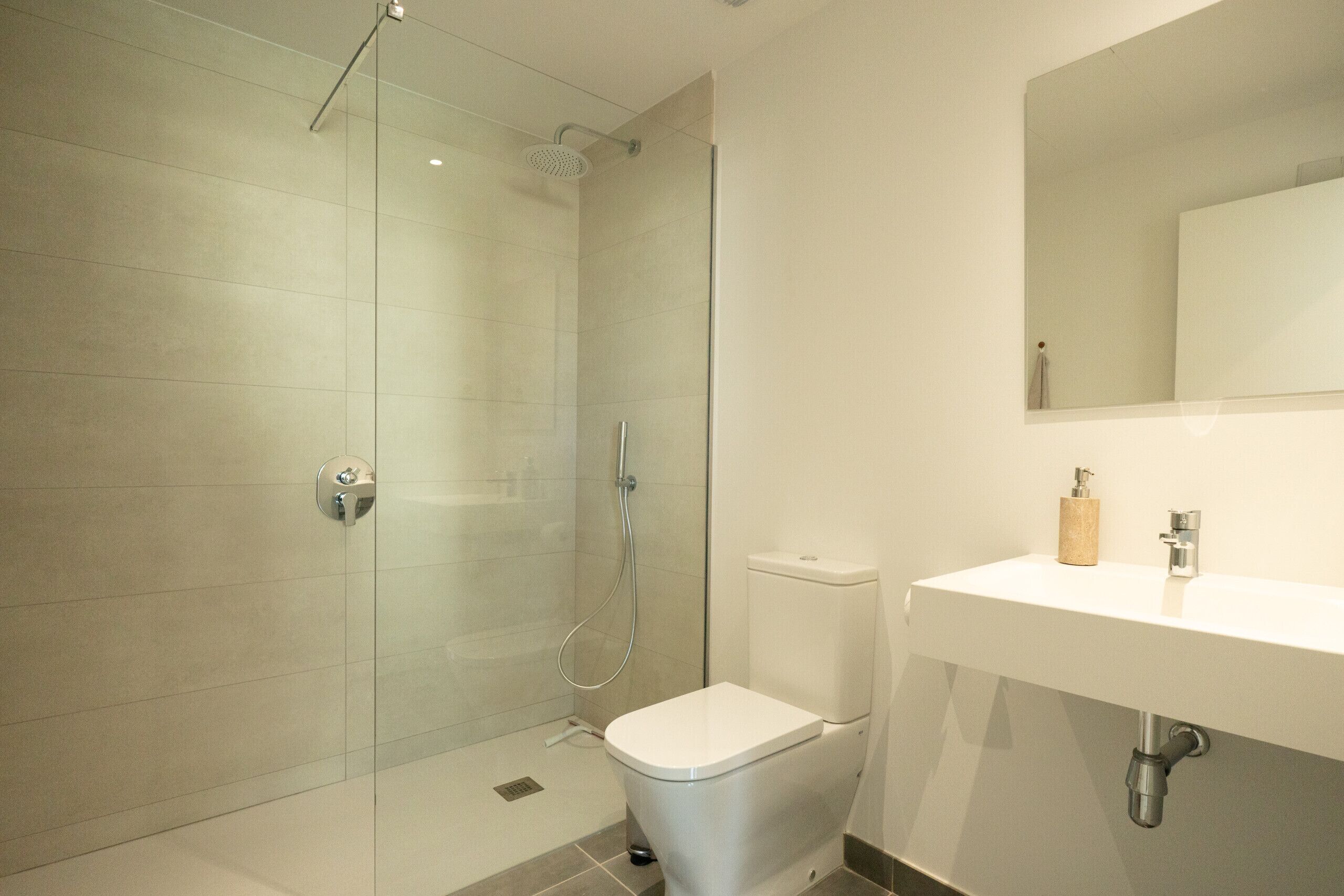 A modern bathroom with a glass-enclosed shower, a white sink, and a toilet.
