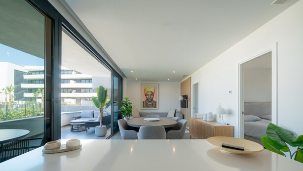 Quarto de hotel moderno com área de refeições, uma grande janela com vista para a cidade, um quadro na parede e uma mesa de cabeceira com abajur.