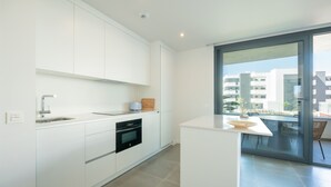 Cozinha moderna com armários brancos, forno embutido e uma grande janela com vista para a cidade.