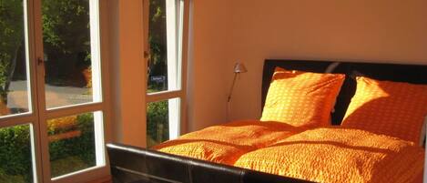 A bedroom with a bed, a bench, and large windows.