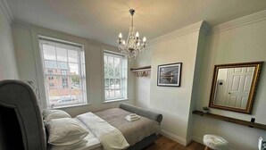 A bedroom with a bed, two windows, a chandelier, a framed mirror, and a small stool. - Historic Old Town Home with Views and free parking (Kingston upon Hull)