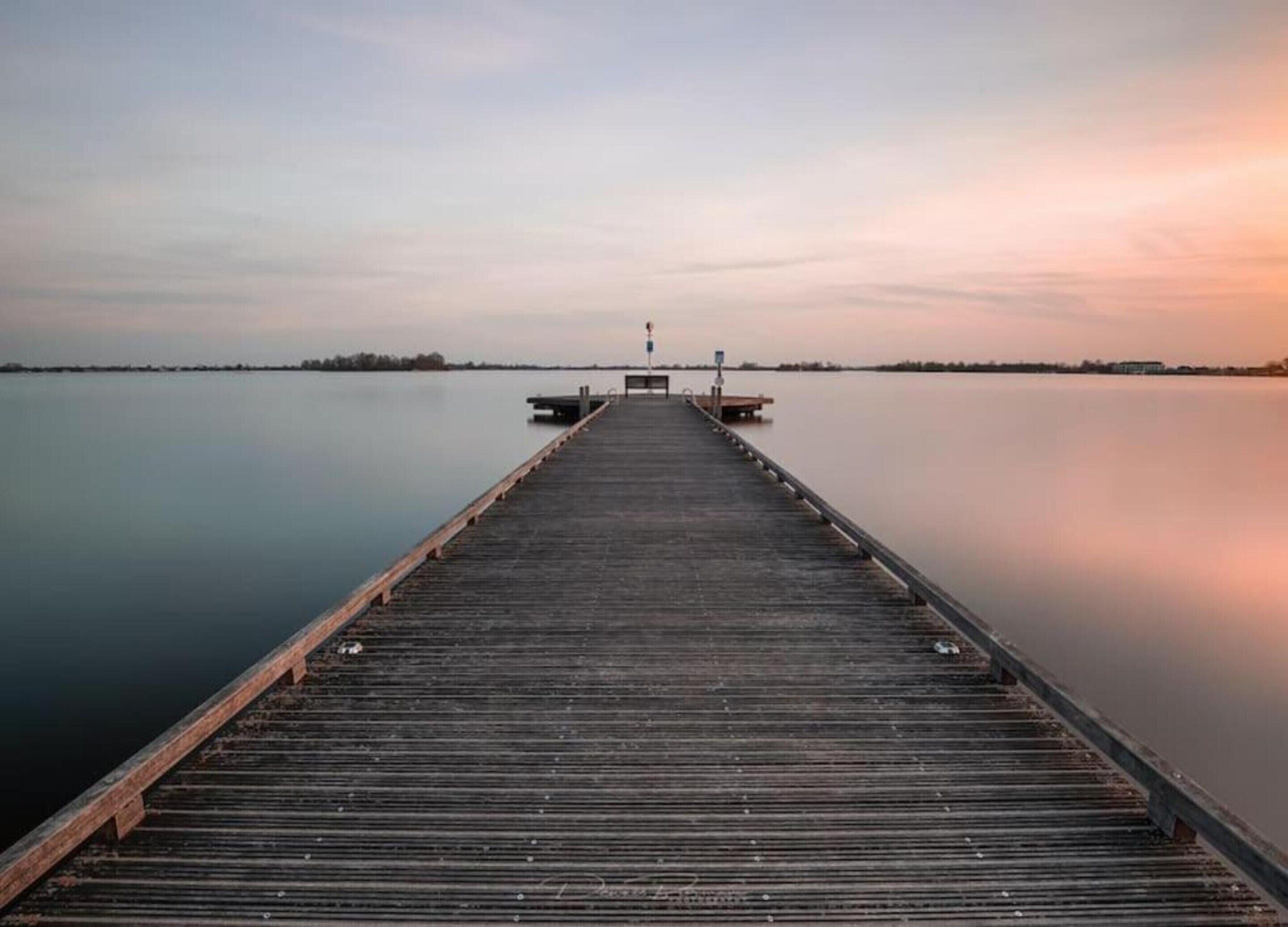 A wooden pier extending into calm water with a bench at the end.