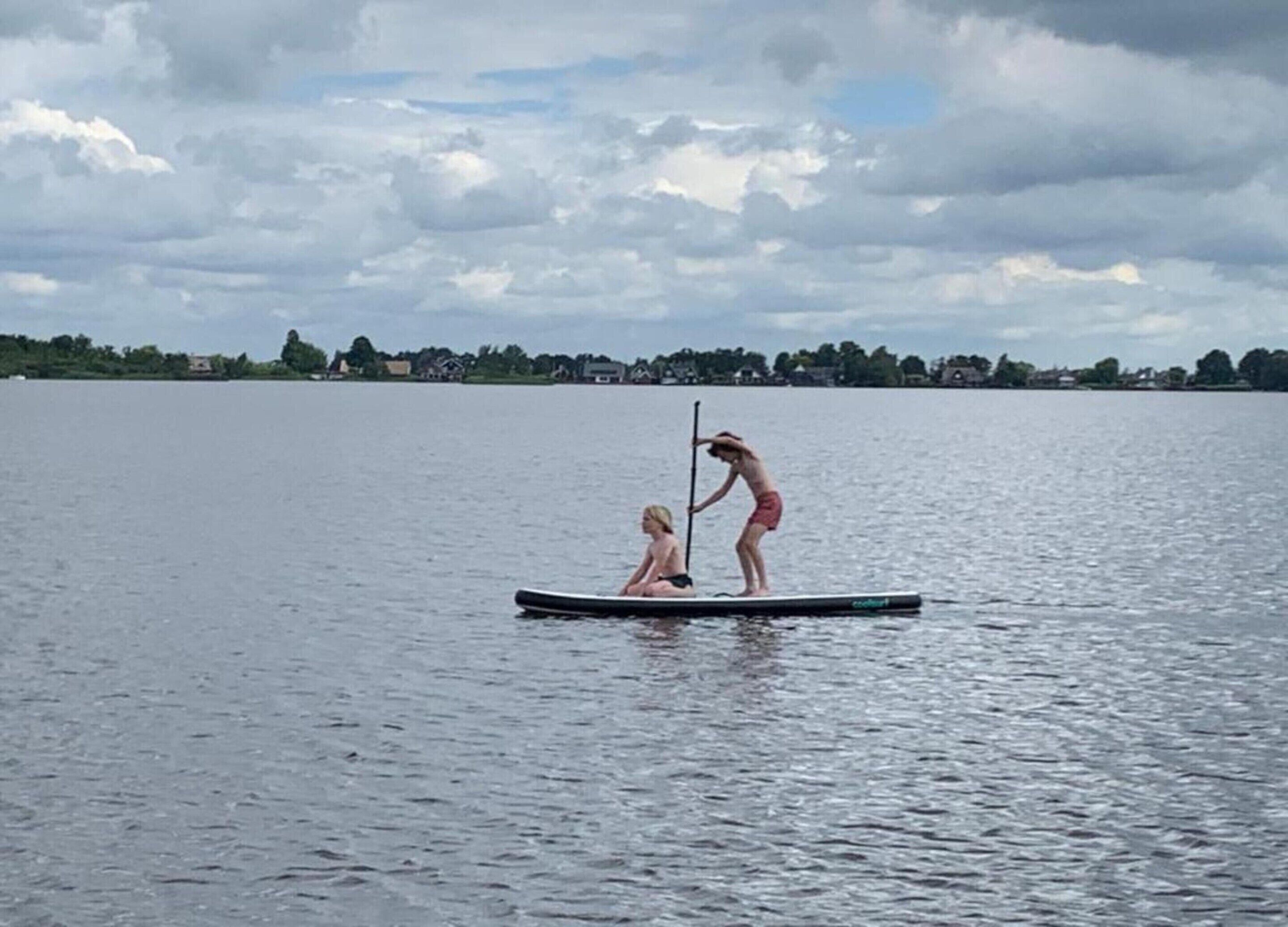 Two people on a paddleboard in a large body of water with a distant shoreline.