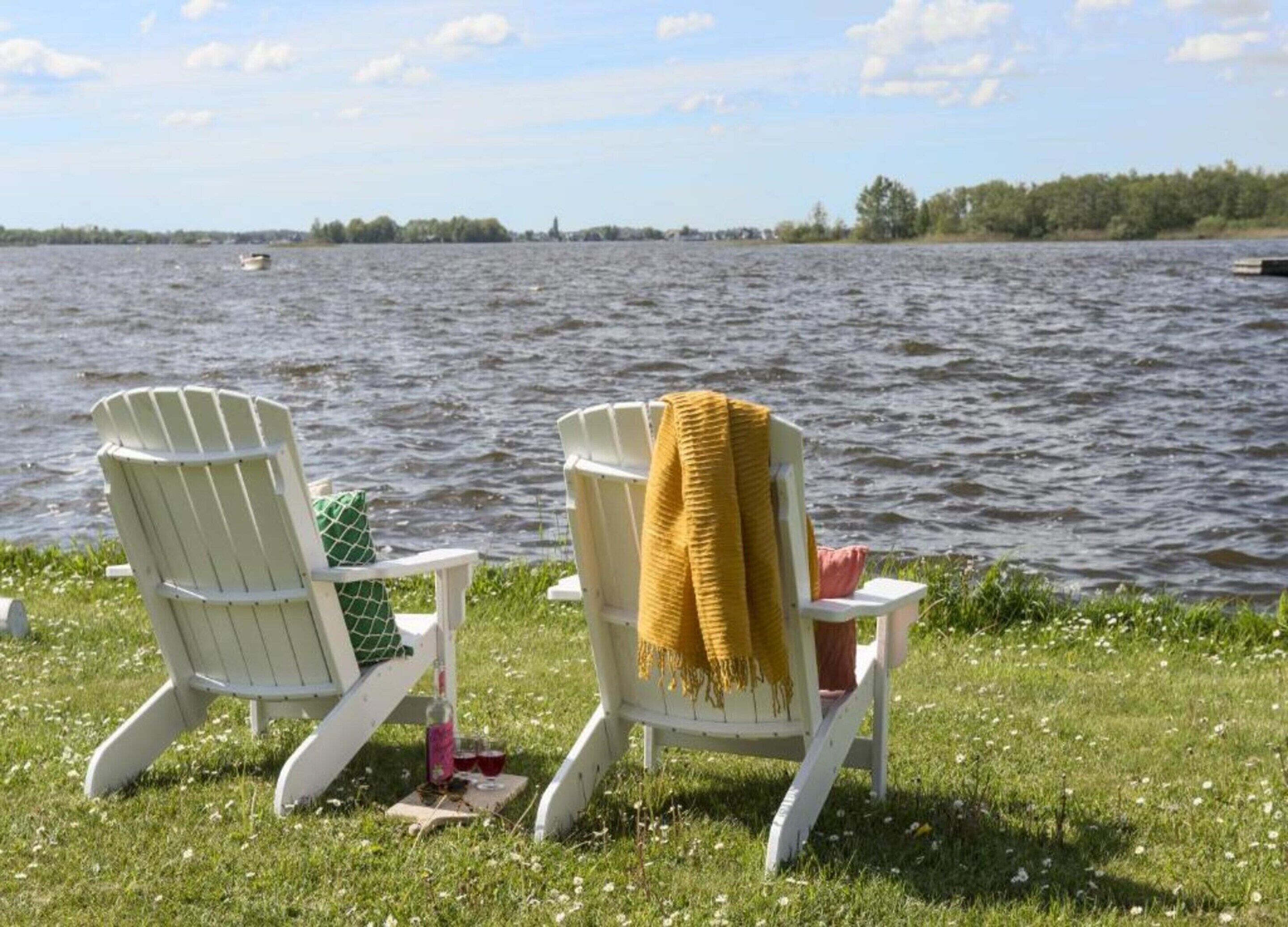 Two Adirondack chairs by a lake with a boat in the distance.
