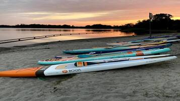 A row of kayaks lined up on a sandy beach with a calm lake in the background.