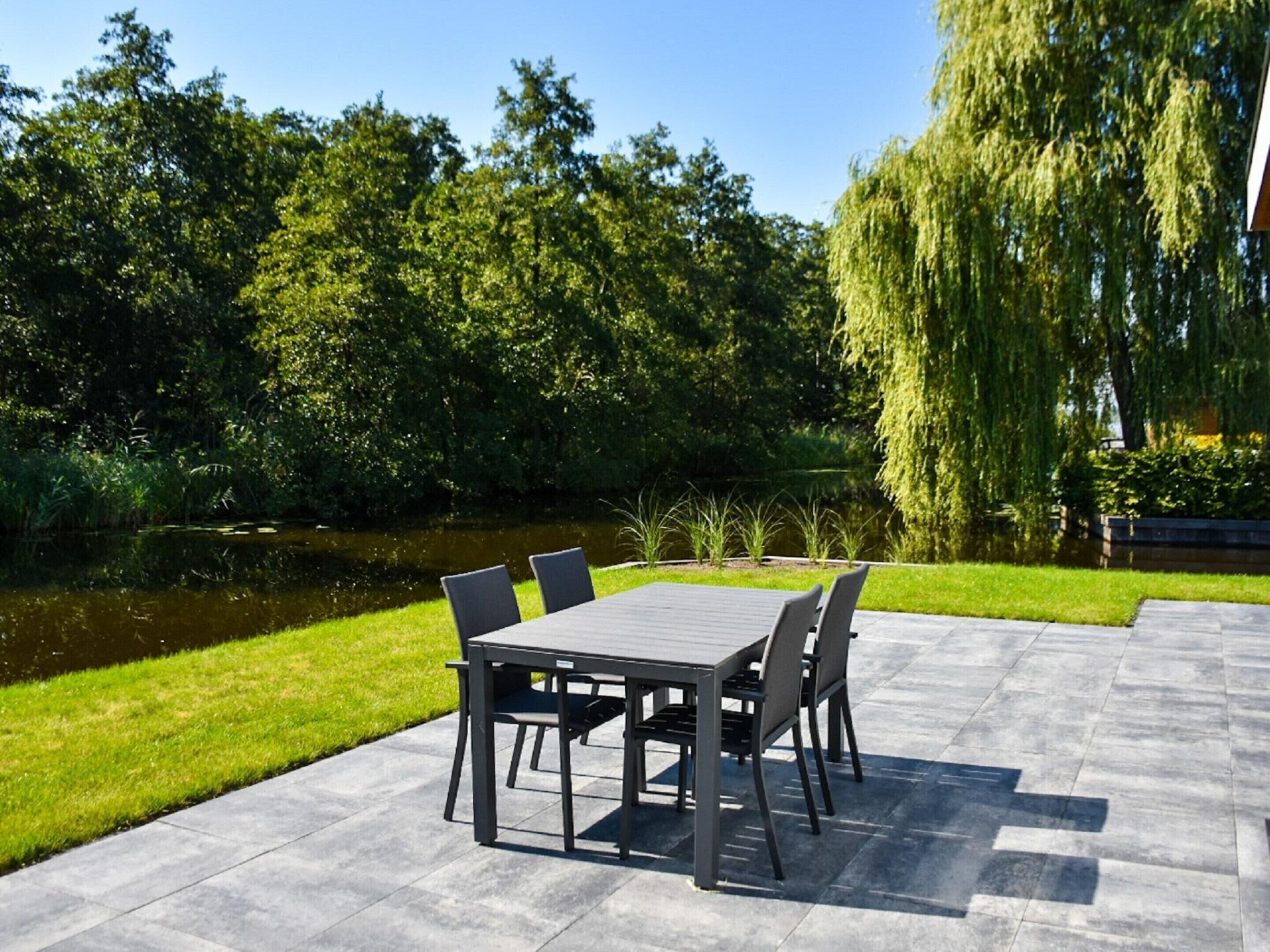 An outdoor patio with a table and chairs, surrounded by a pond and trees.