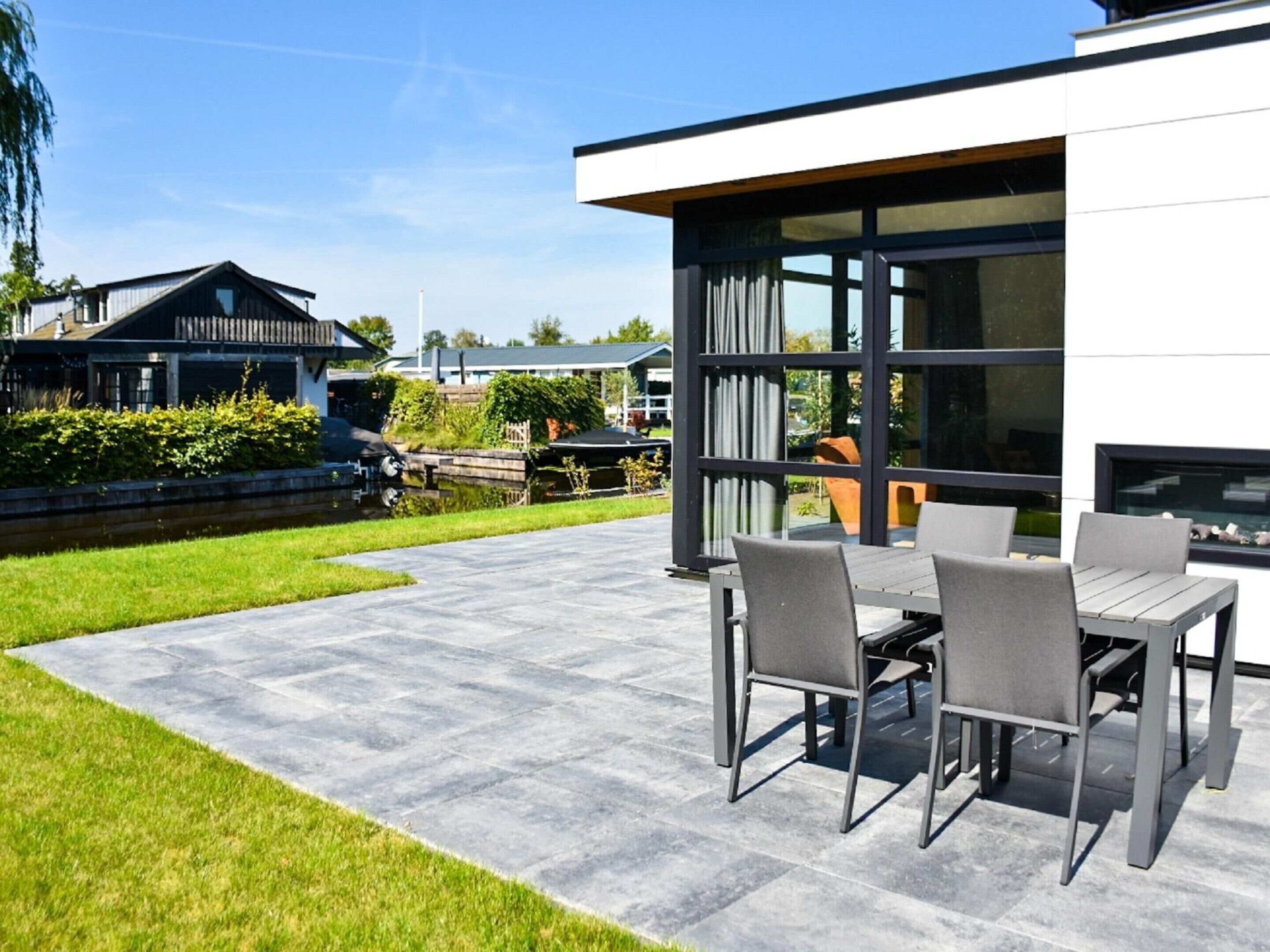 A modern outdoor patio with a table and chairs, a swimming pool, and a view of a residential area.