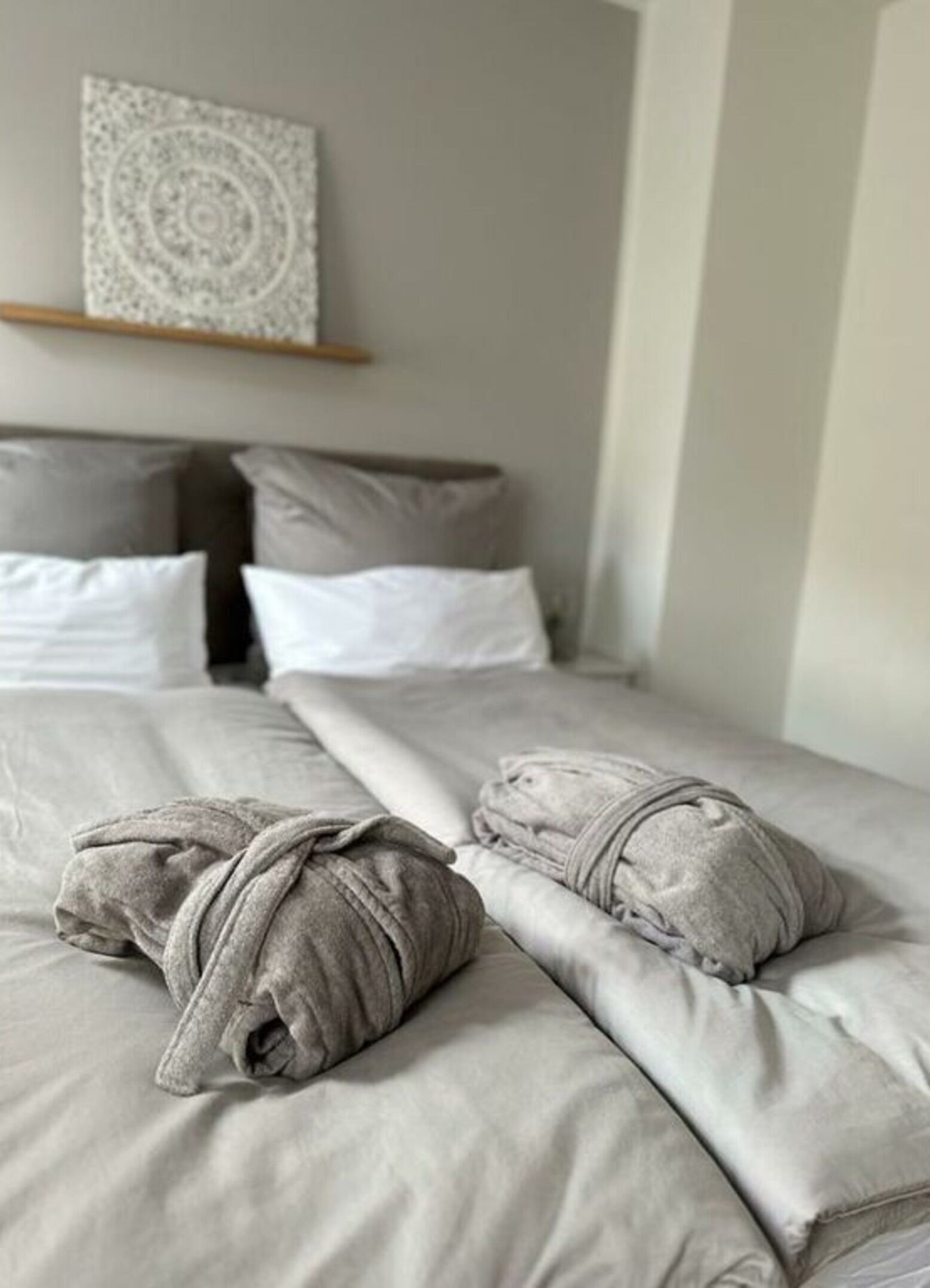 A neatly made bed with grey bedding and two rolled-up towels.
